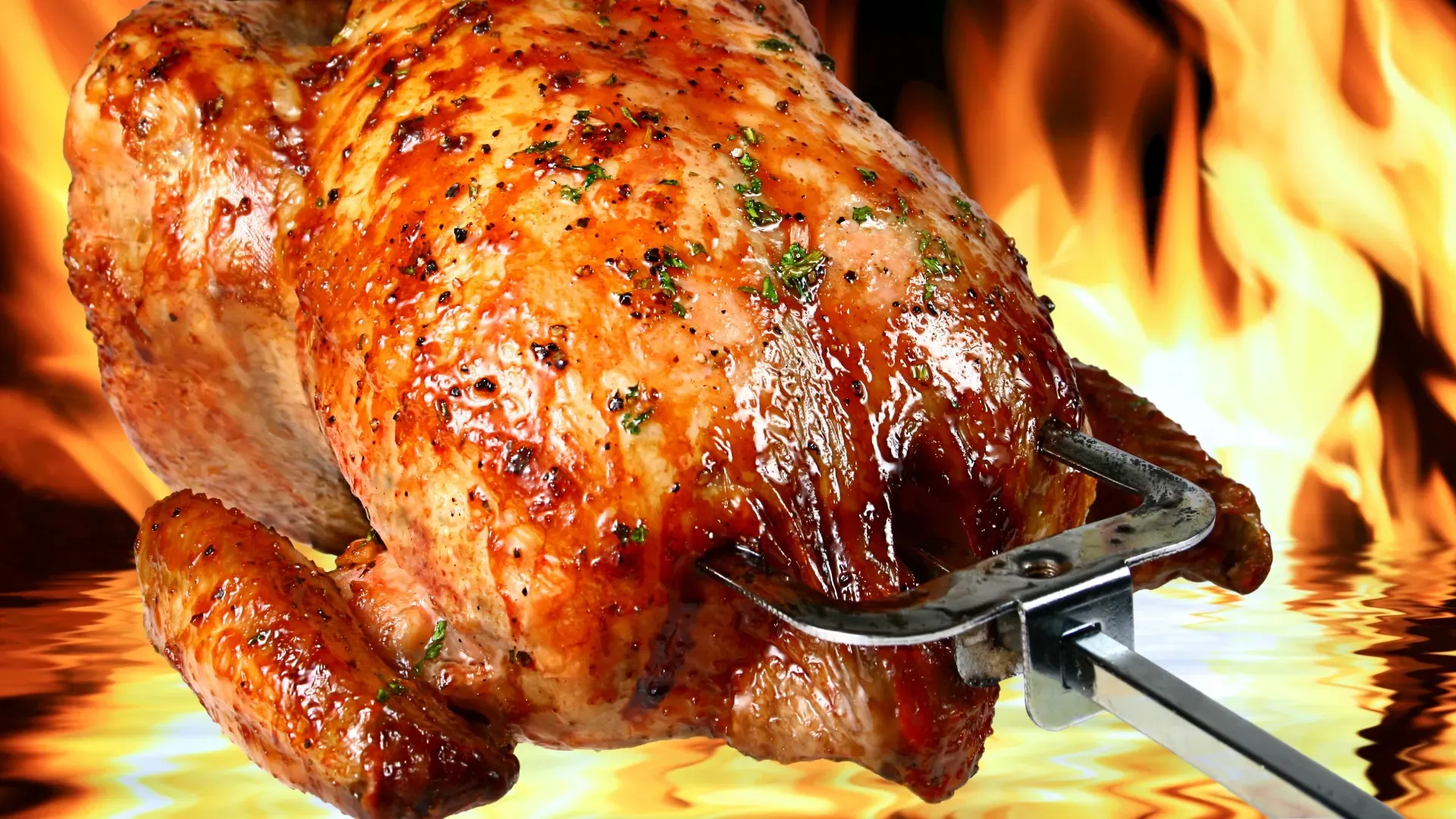 A roasted chicken on a skewer with flames in the background