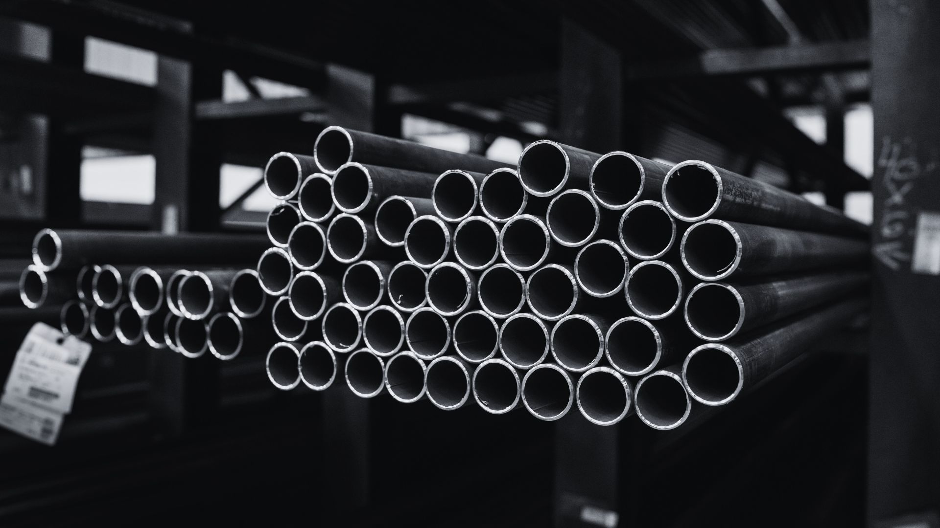 A stack of industrial metal pipes arranged in rows on a rack in a warehouse setting.