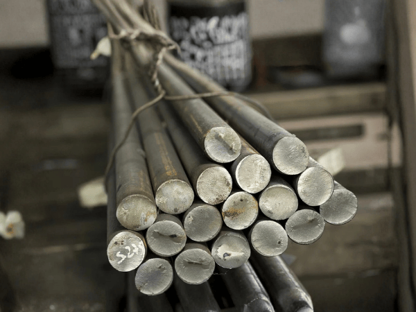 A bundle of grey metal rods stacked together, viewed from the end, tied with wire in a workshop setting.