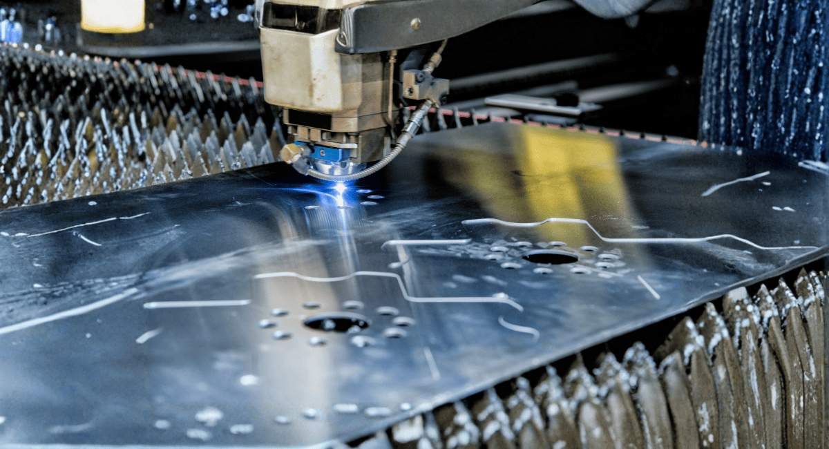 A laser cutting machine cuts intricate patterns into a metal sheet resting on a spiky industrial bed.