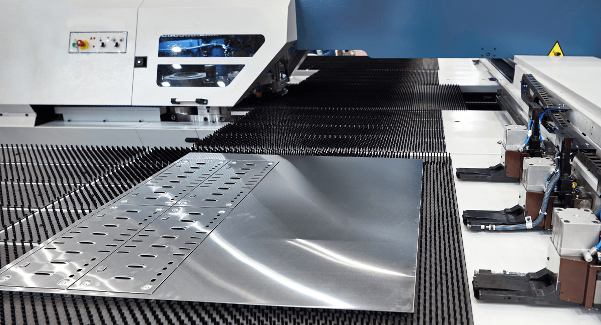 A metal sheet with punched patterns moves through an industrial laser cutting machine.