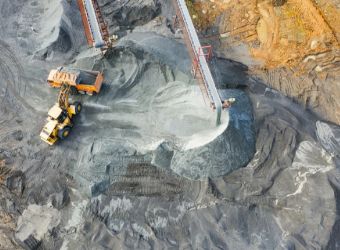 Aerial view of quarry; yellow machinery loads gray gravel from conveyor belts into orange dump truck.