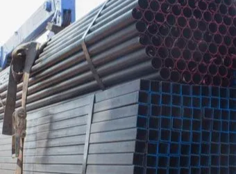 A flatbed truck loaded with stacks of circular and square metal tubing secured by a heavy-duty strap.