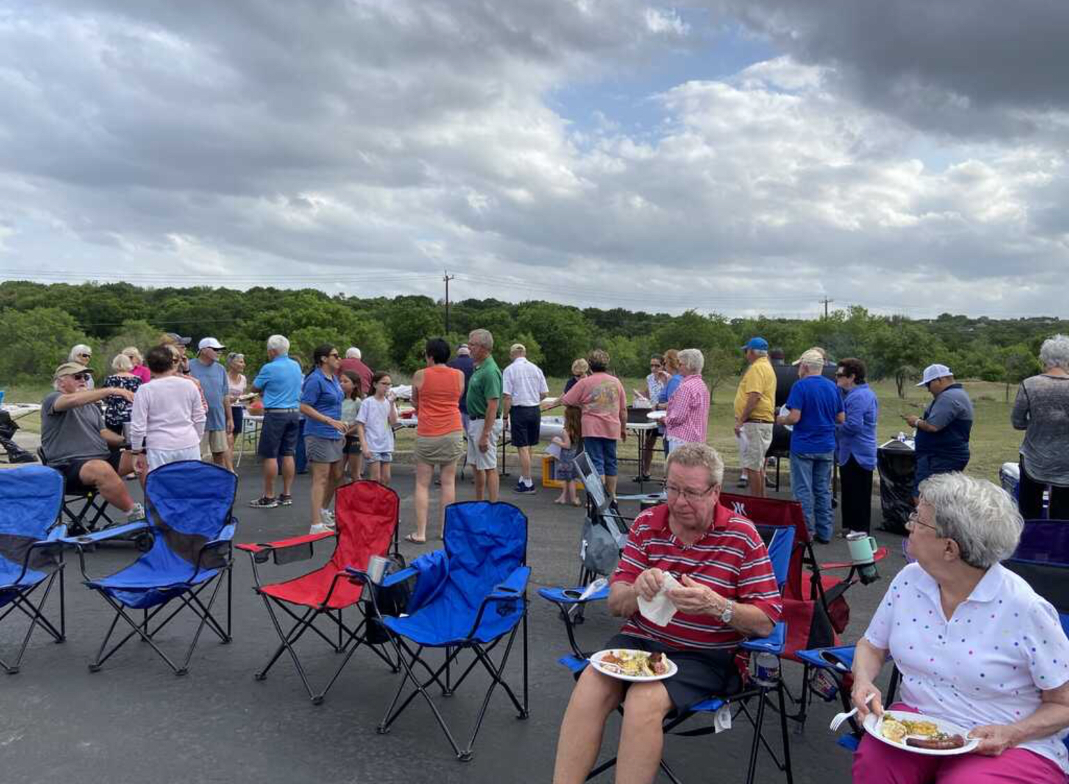 A group of people are sitting in folding chairs eating food.