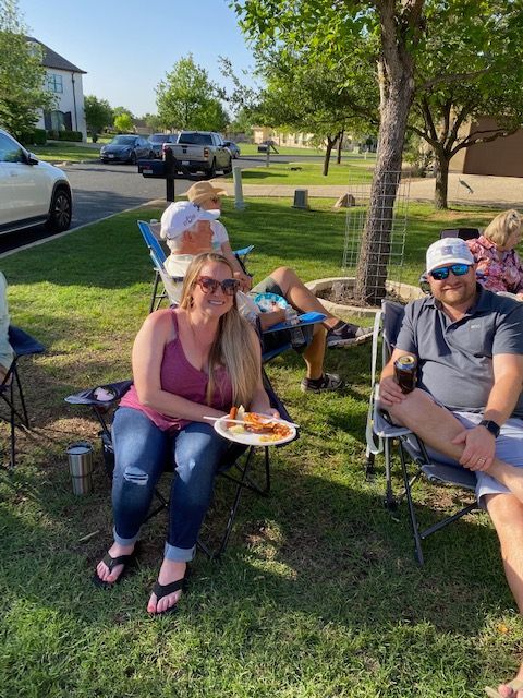 A woman is holding a plate of food while sitting in the grass with other people.
