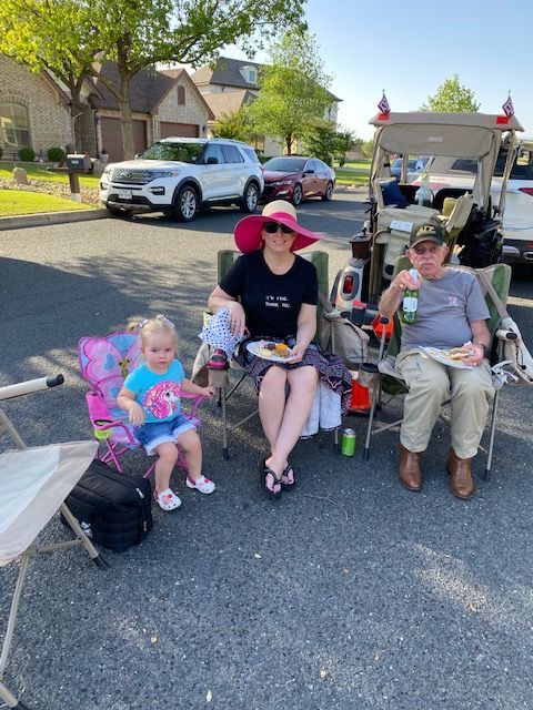 A group of people are sitting in chairs in a parking lot eating food.