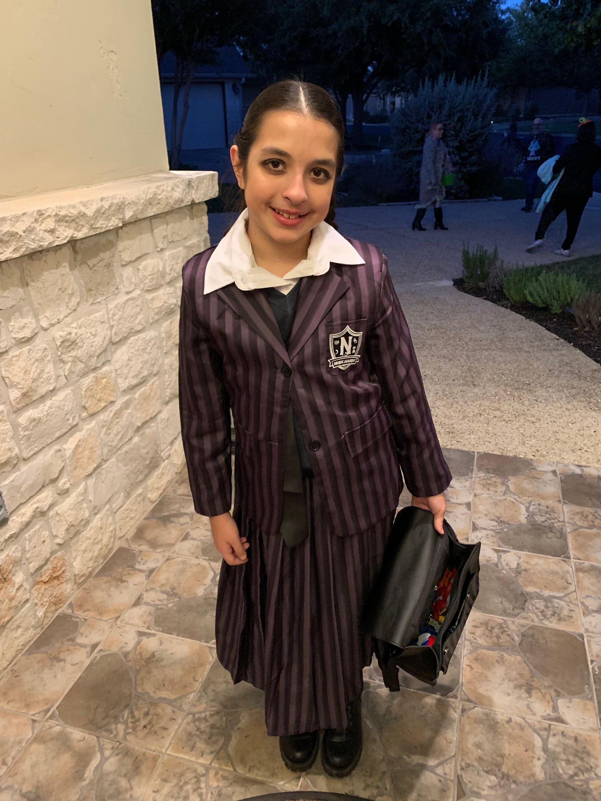 A little girl is wearing a purple suit and holding a black briefcase.