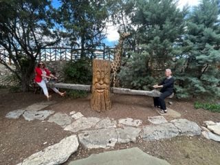 Two people are sitting on a bench next to a statue of a giraffe.