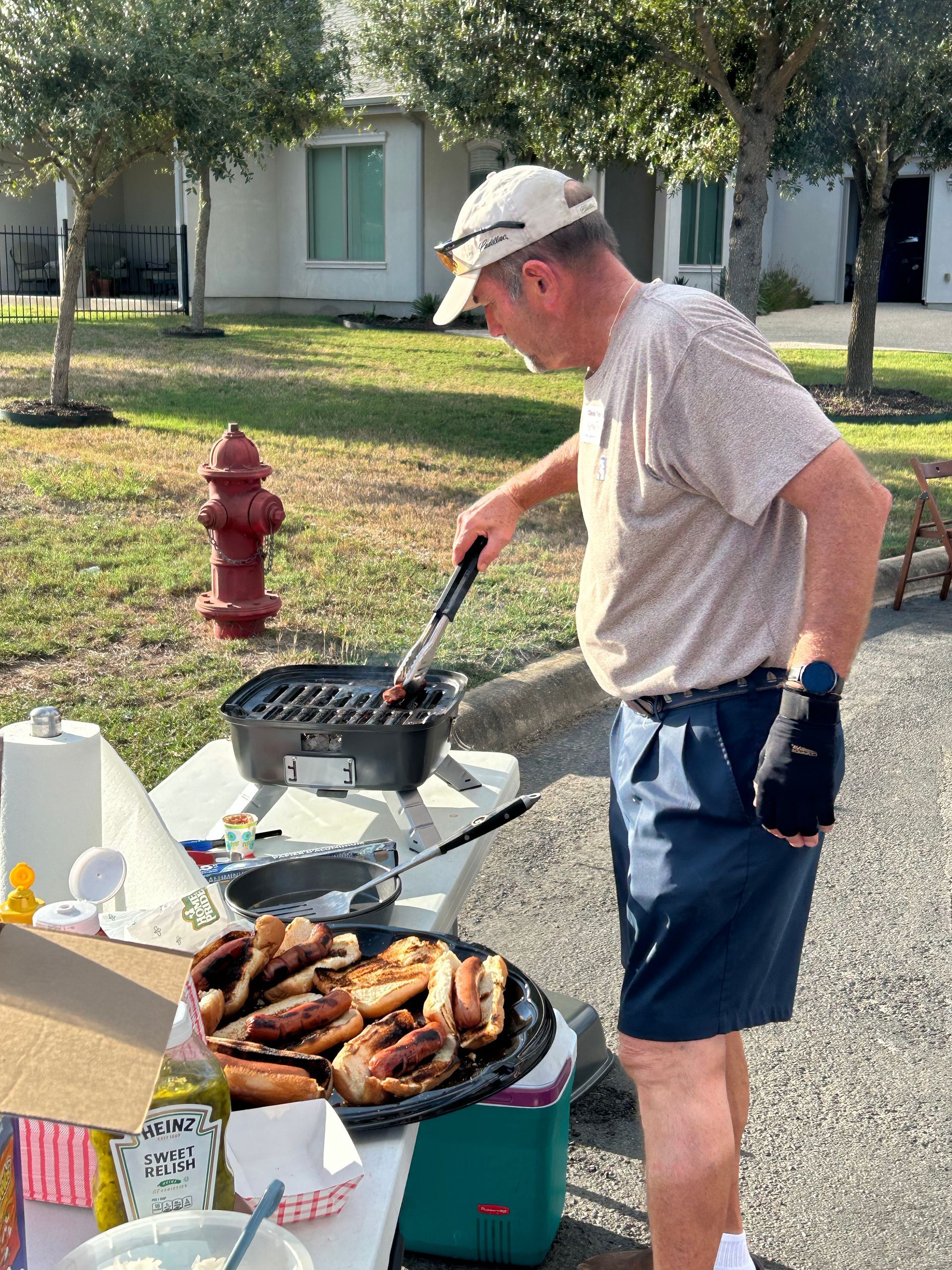 A man is cooking food on a grill in front of a fire hydrant.