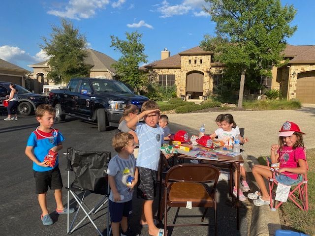 A group of children are sitting around a table in a driveway.
