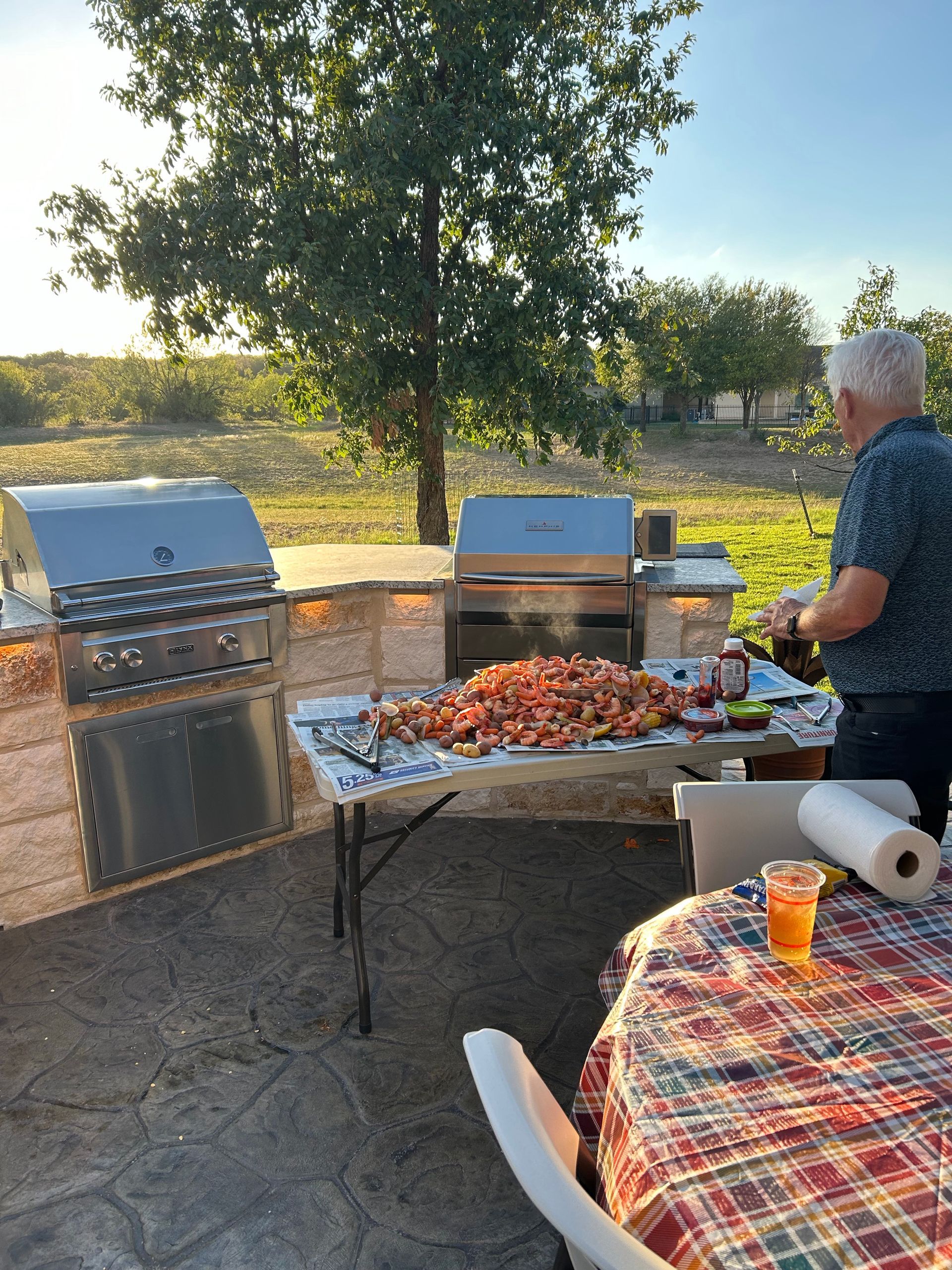 A man is standing in front of a grill and a table with food on it.