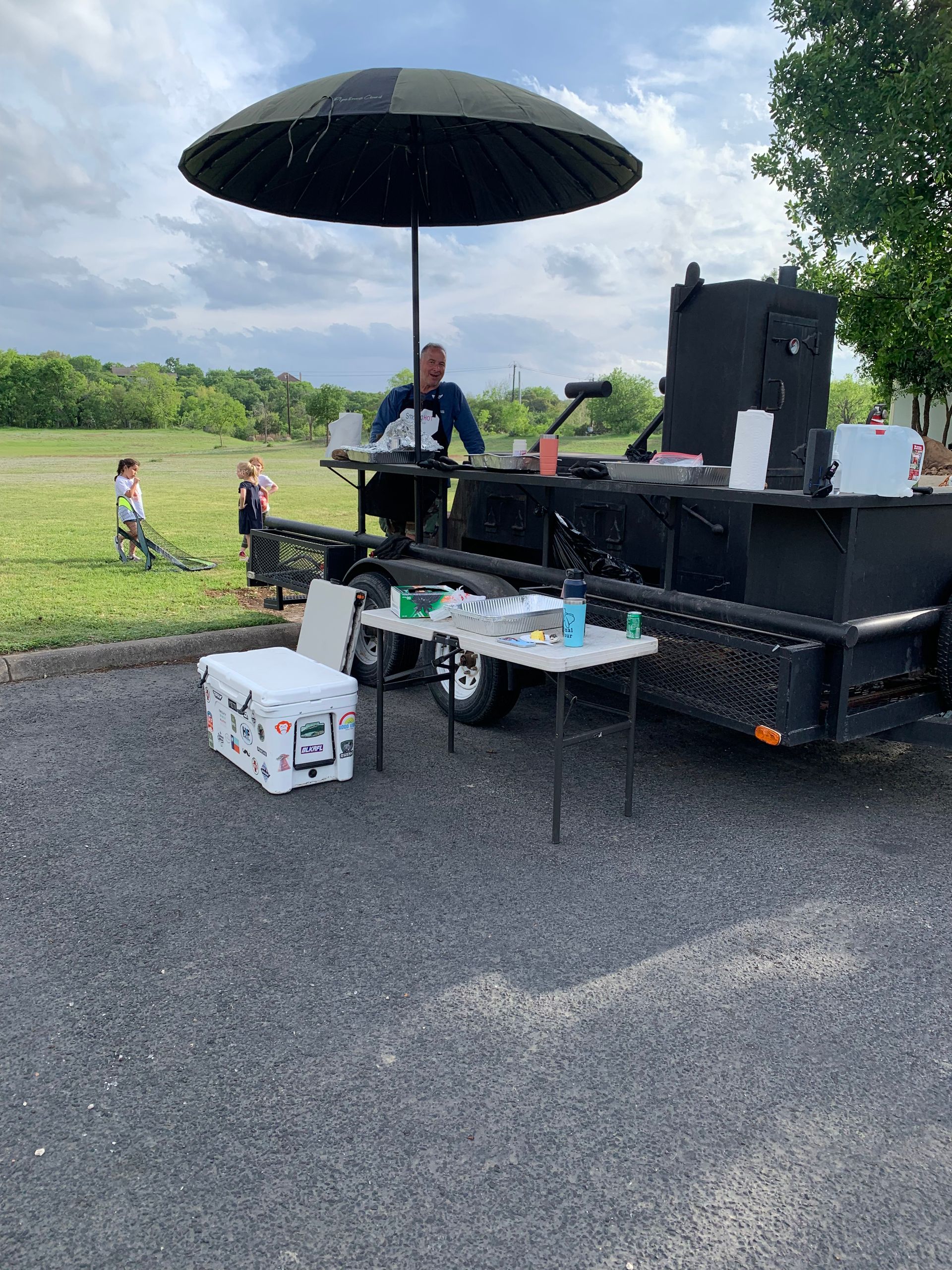 A man is sitting at a table under an umbrella in front of a trailer.