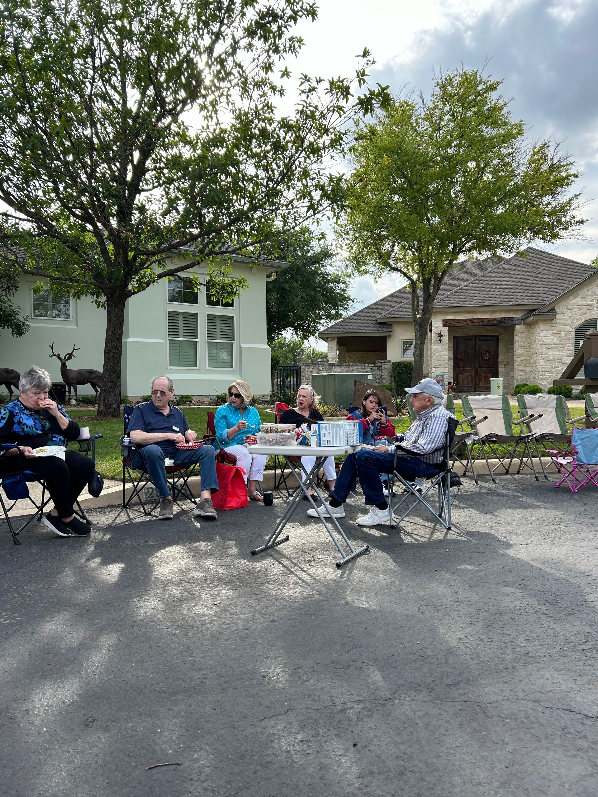 A group of people are sitting around a table in a parking lot.