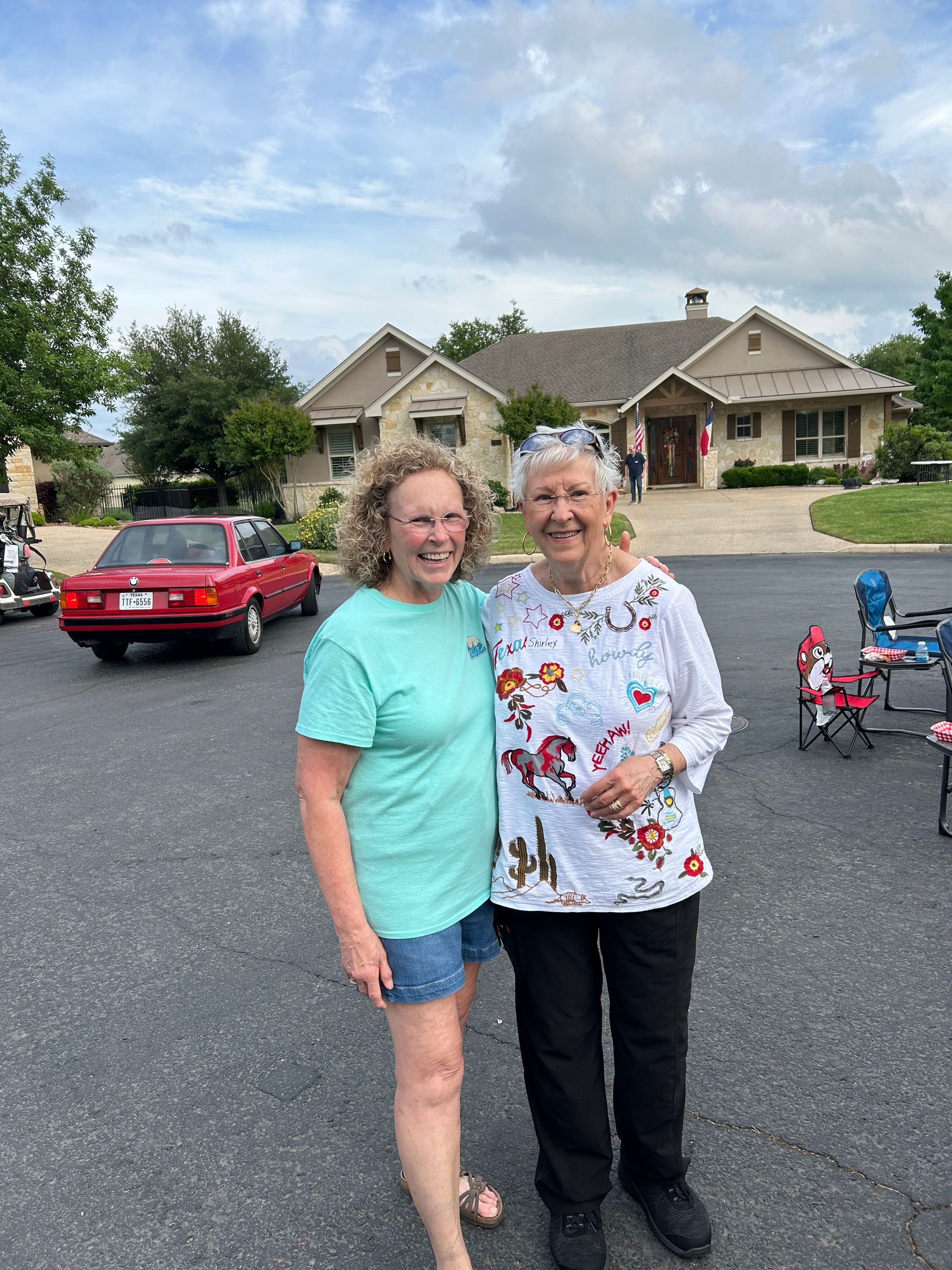 Two women are standing next to each other in front of a house.