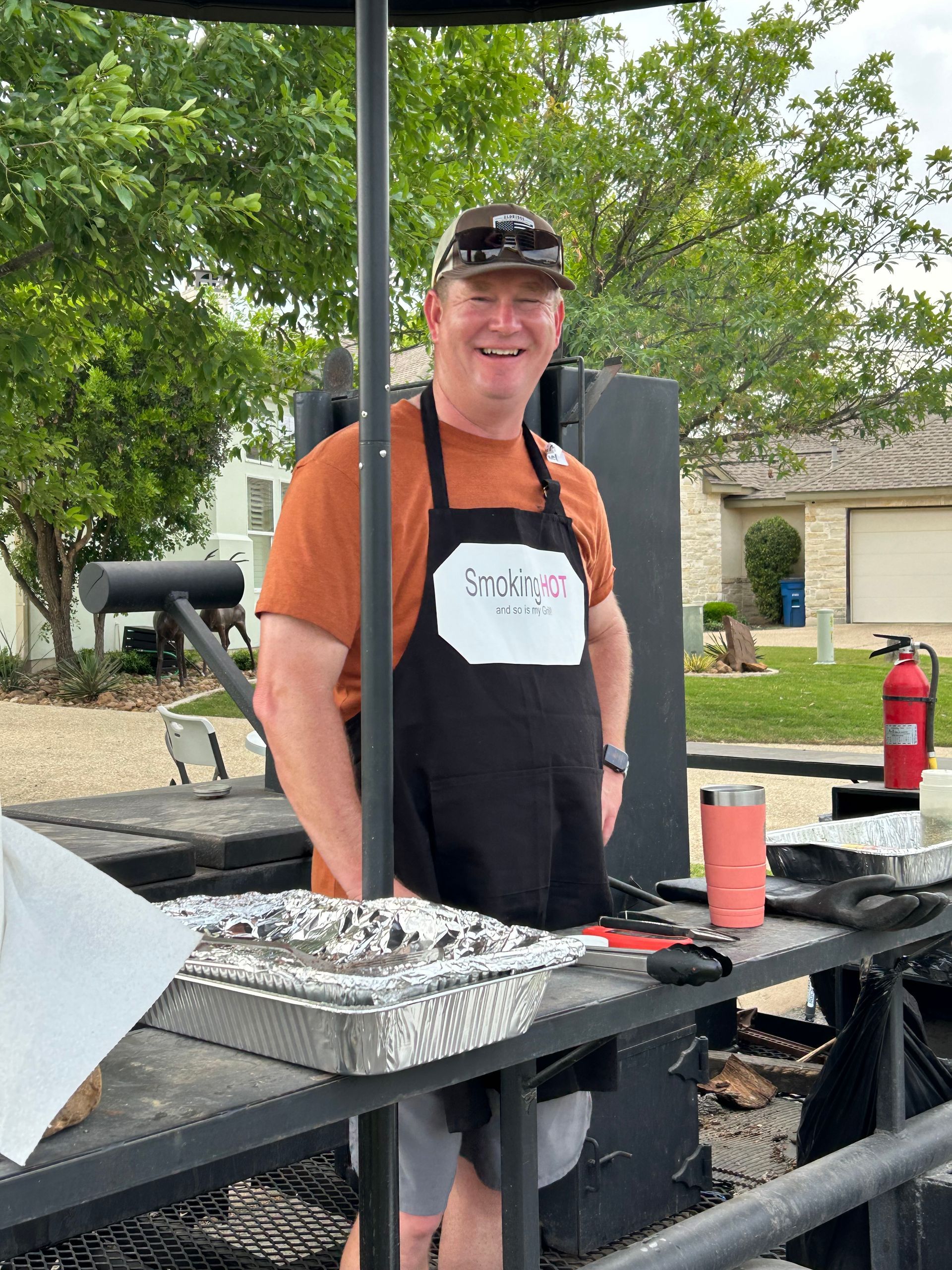 A man wearing an apron is standing in front of a grill.
