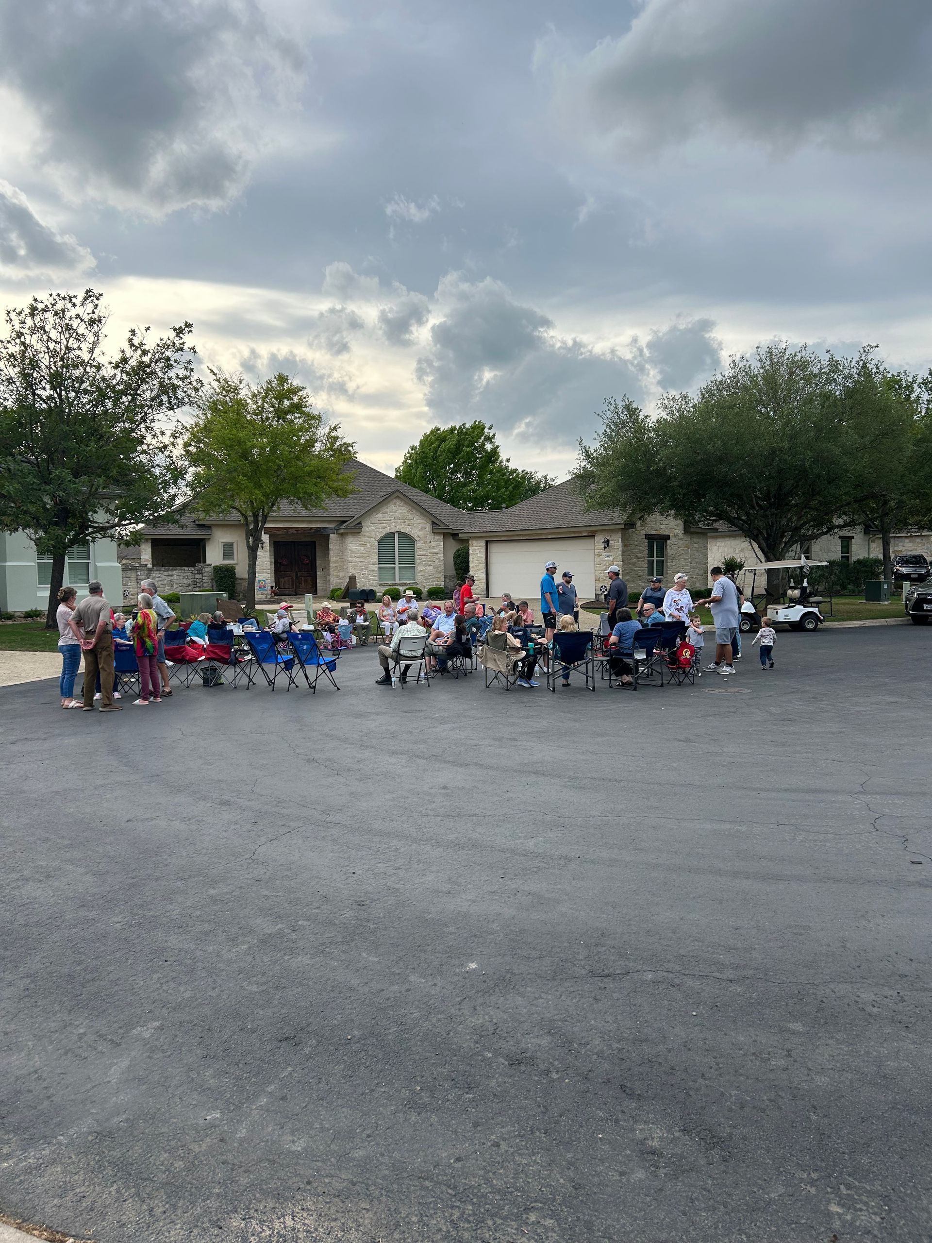 A group of people are gathered in a parking lot in front of a house.