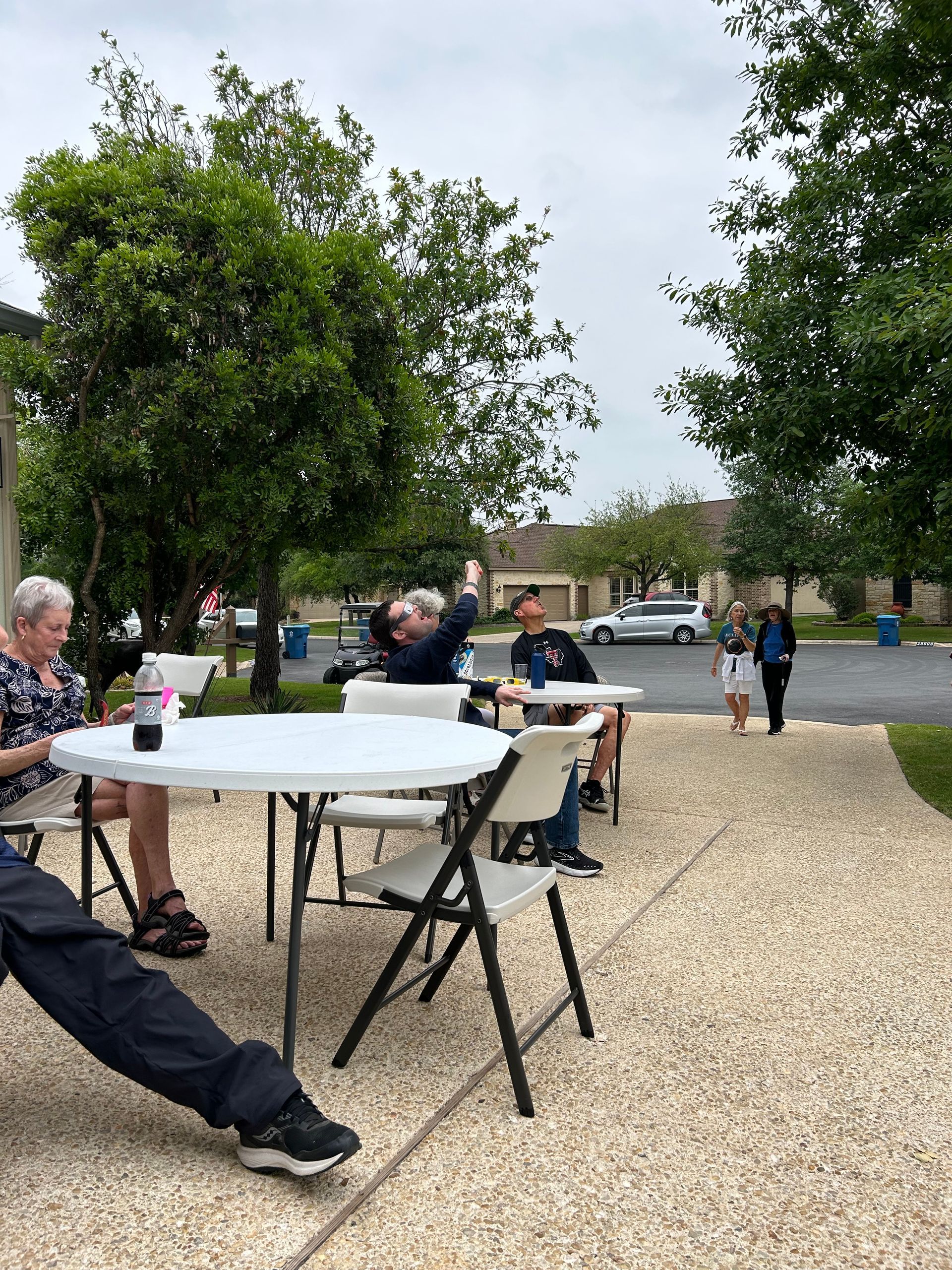 A group of people are sitting at tables in a parking lot.