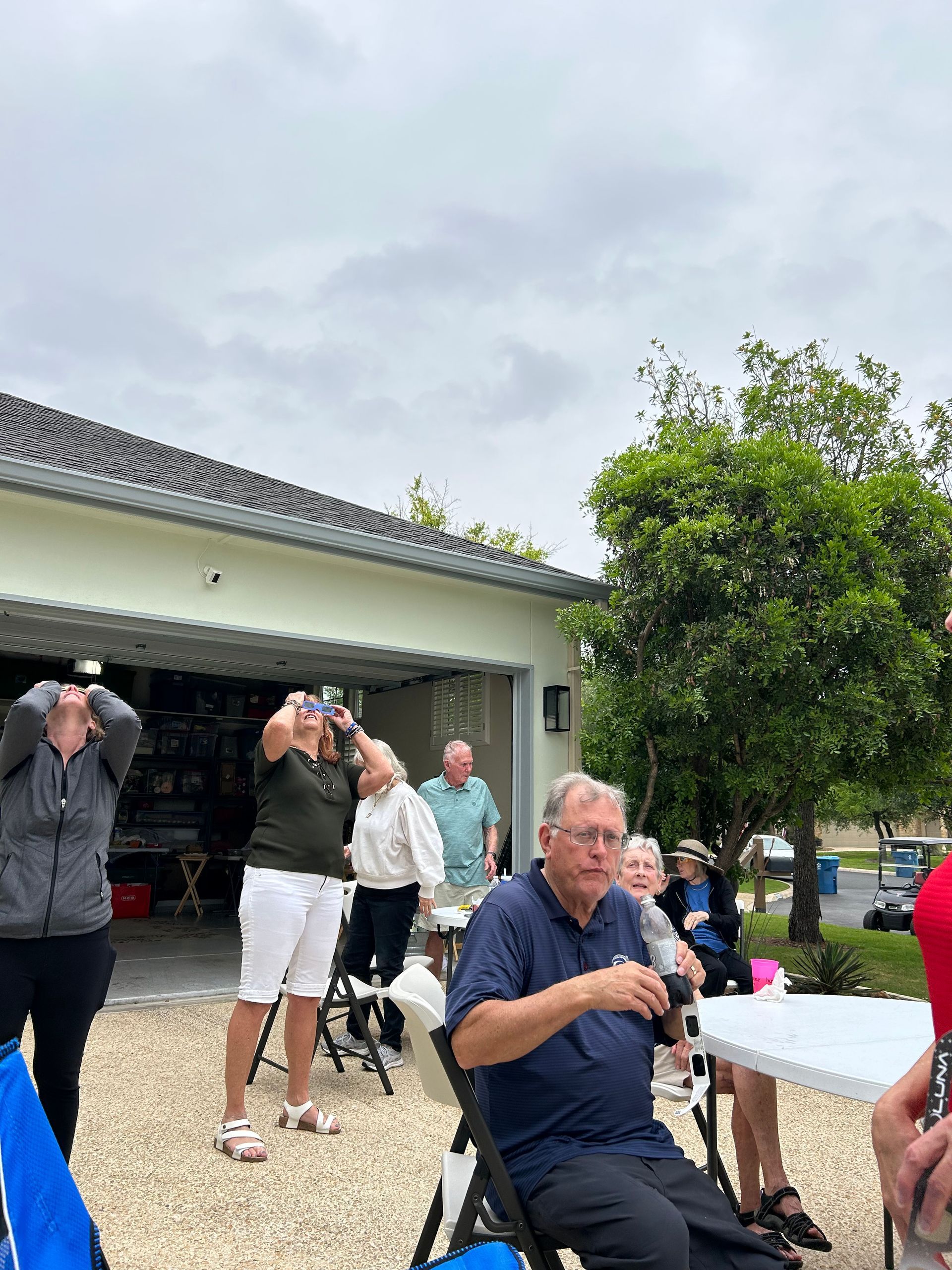 A group of people are sitting at tables in front of a garage.