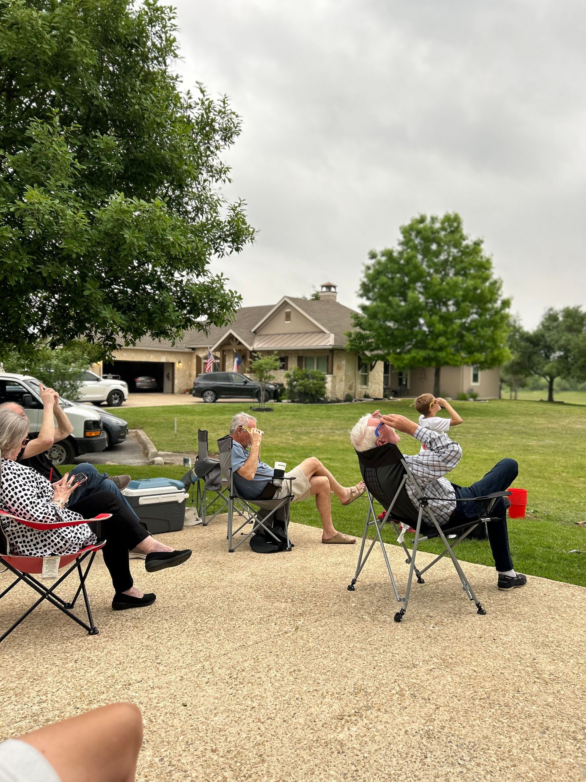 A group of people are sitting in folding chairs in front of a house.