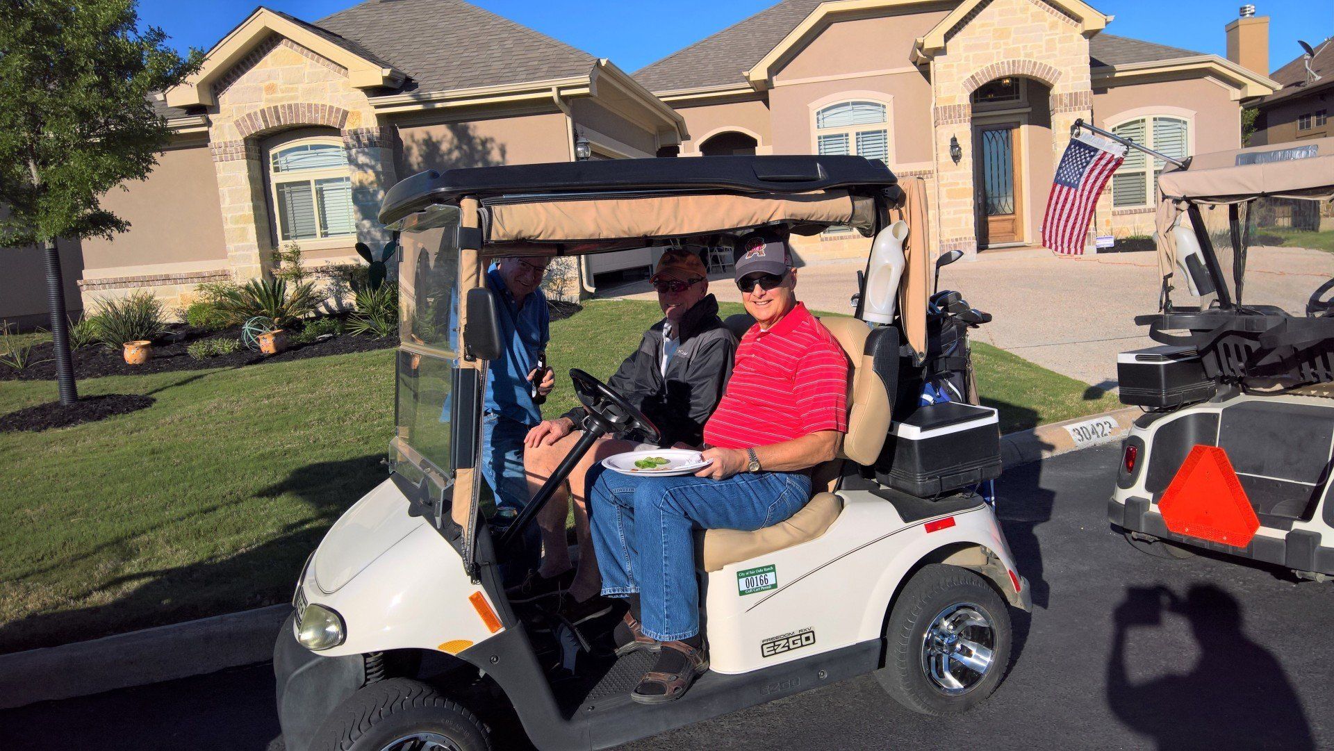 Two men are sitting in a golf cart in front of a house.