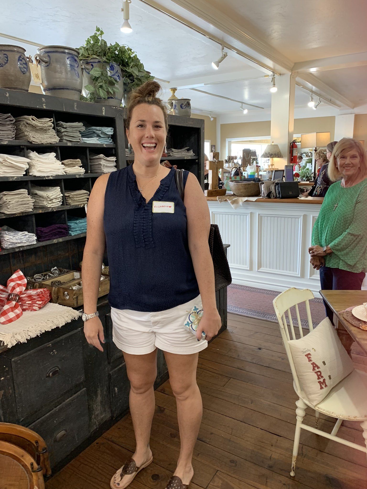 A woman in a blue tank top and white shorts is standing in a store.