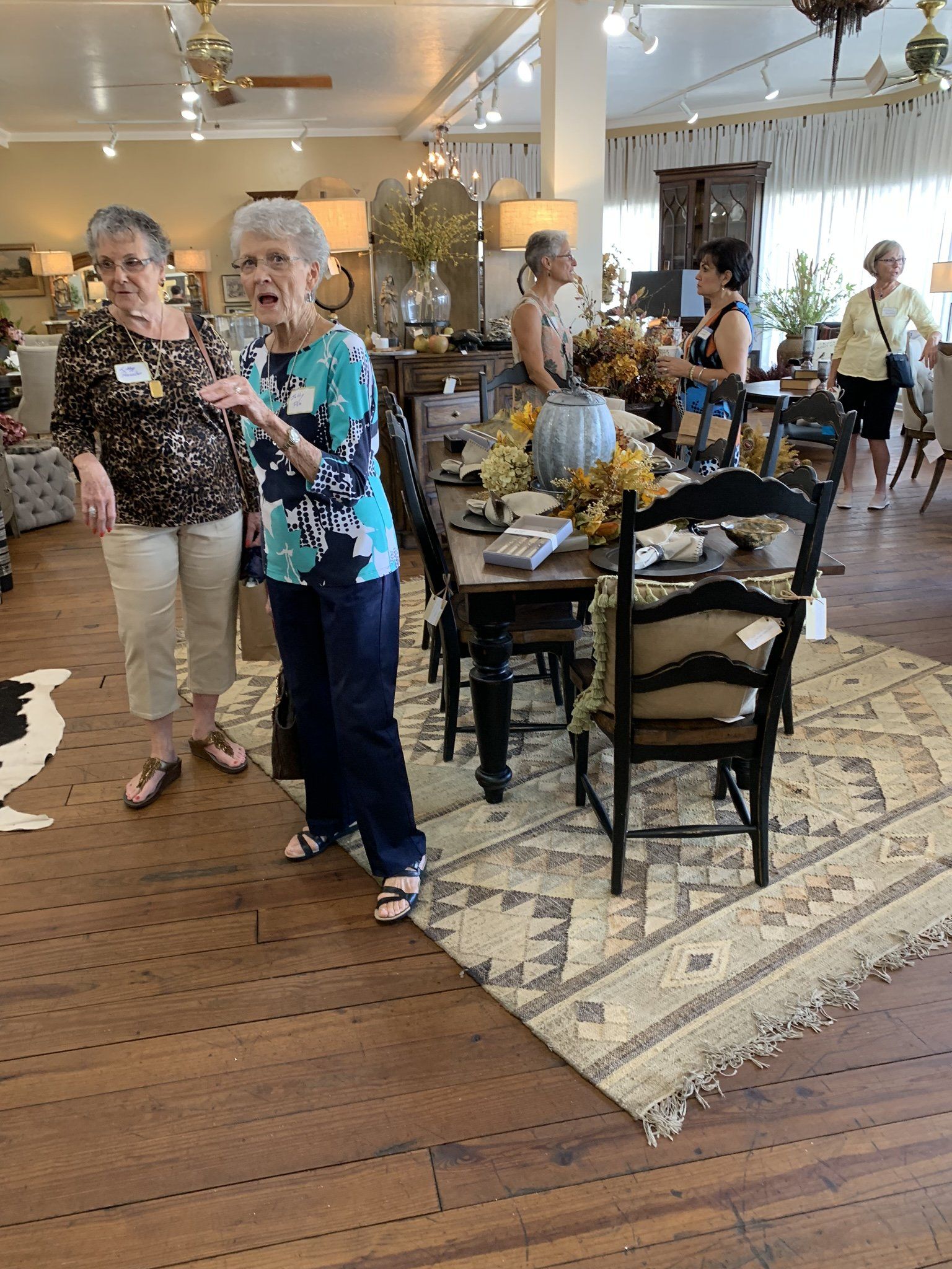 A group of women are standing in a room with a table and chairs.