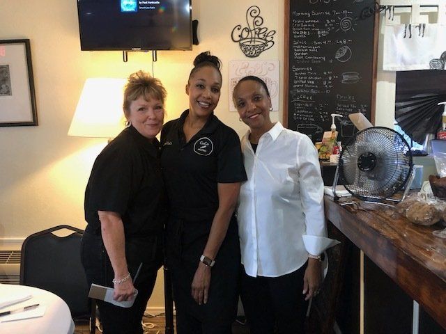 Three women are posing for a picture in front of a sign that says coffee