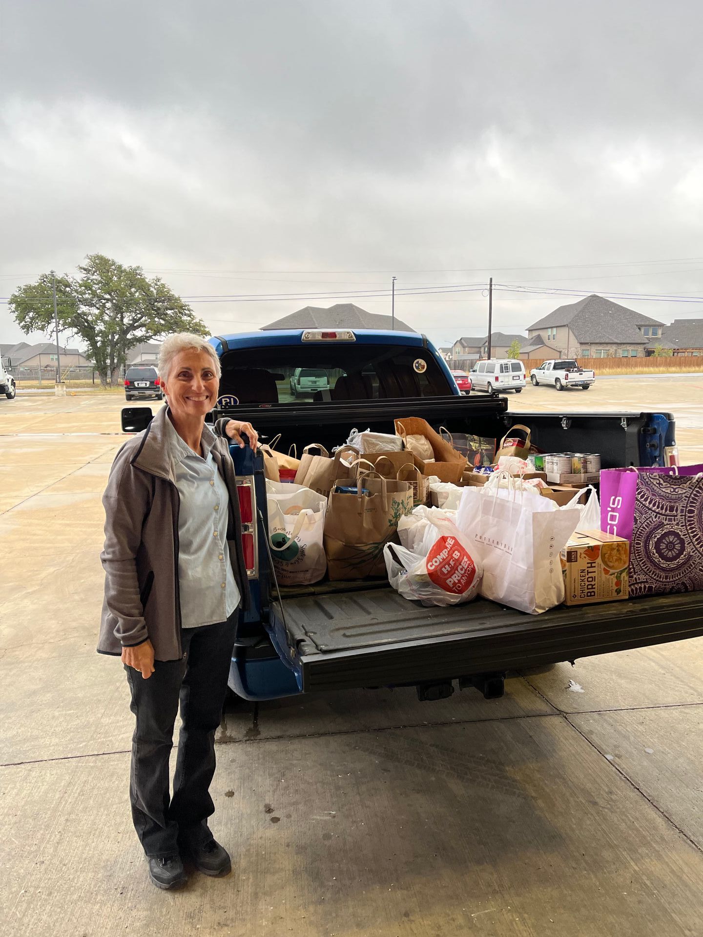 A woman is standing in front of a truck filled with bags of food.