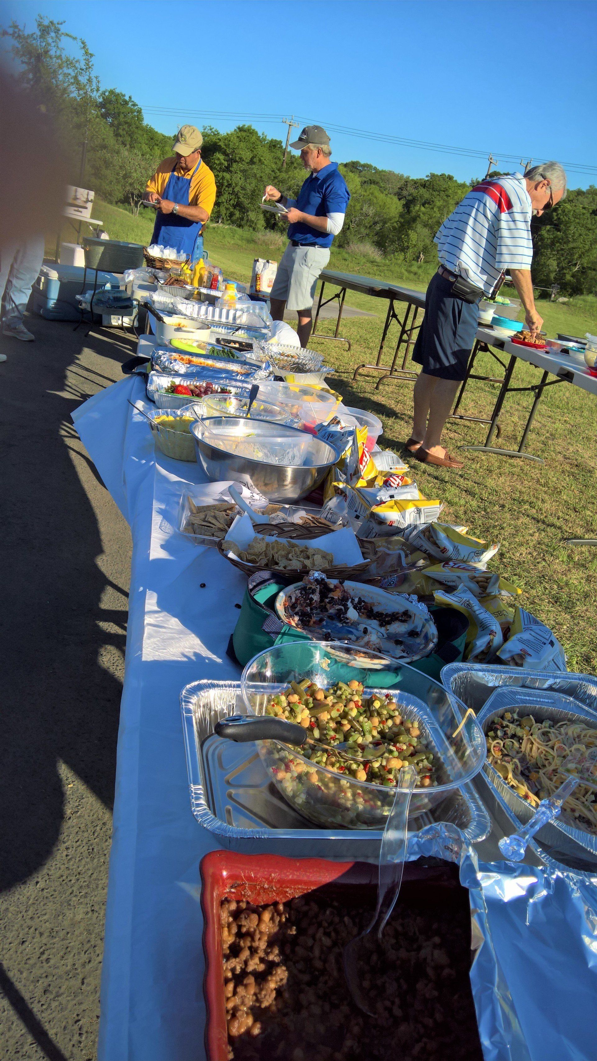 A long table filled with lots of food and people standing around it.