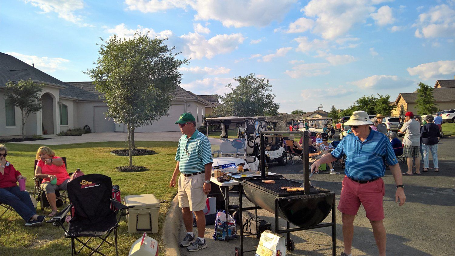 A group of people are standing around a grill in a driveway.