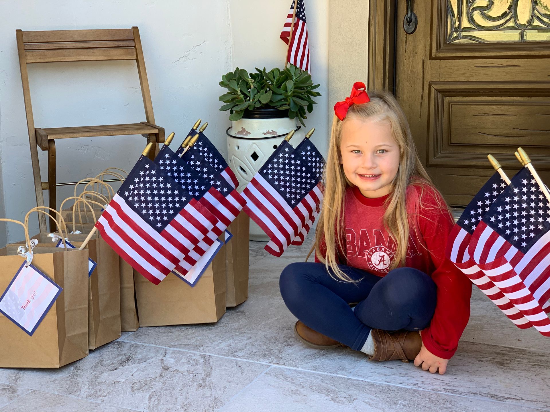 A little girl is sitting on a porch holding american flags.