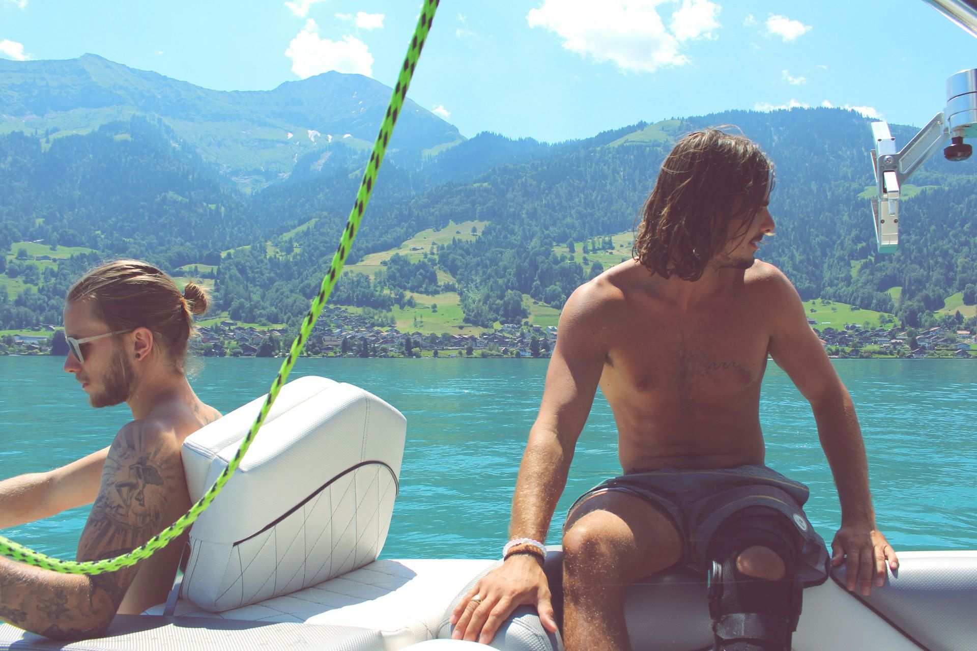 Two men are sitting on a boat in the water with mountains in the background