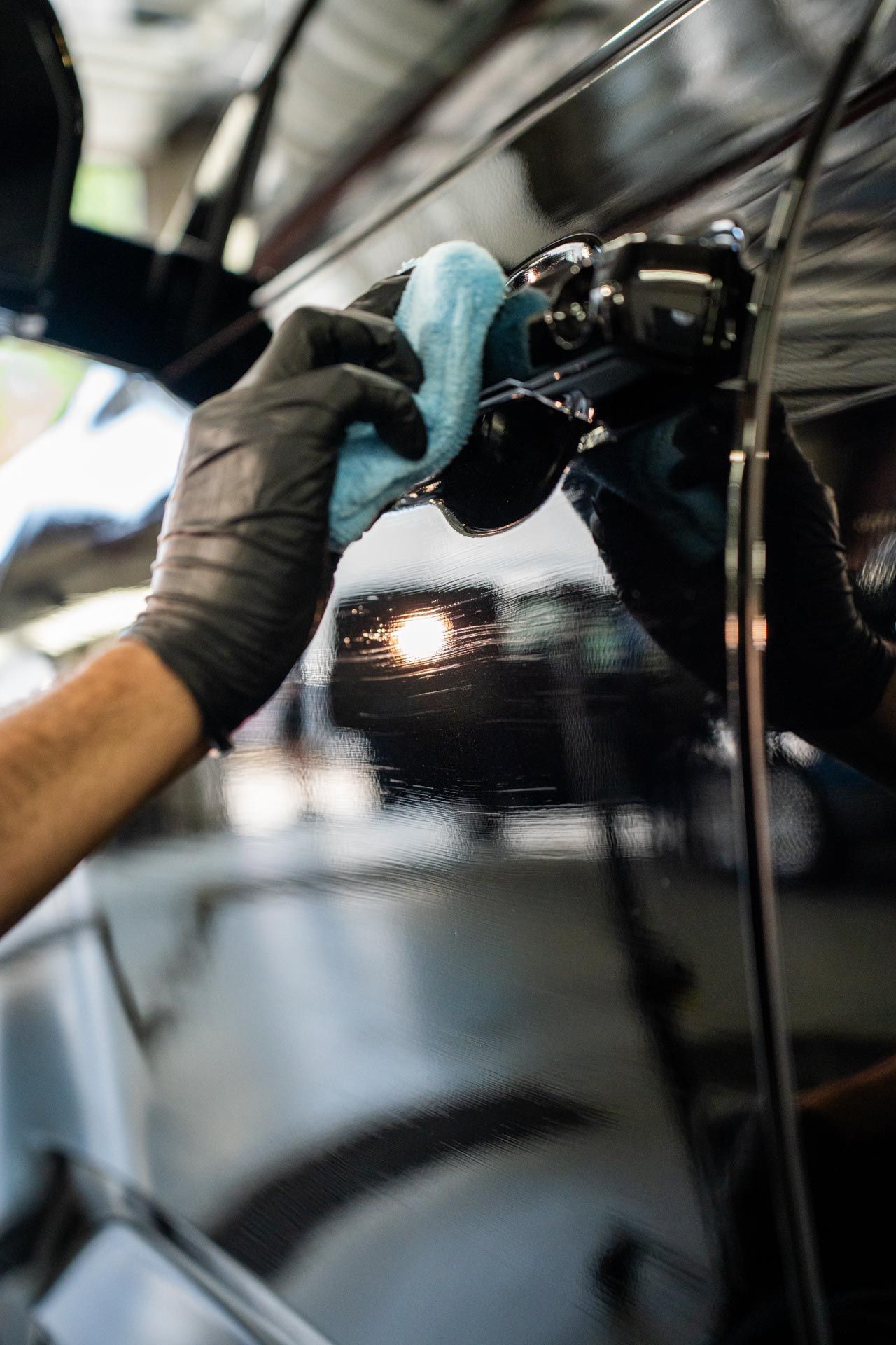 A person wearing black gloves is cleaning a car with a cloth.