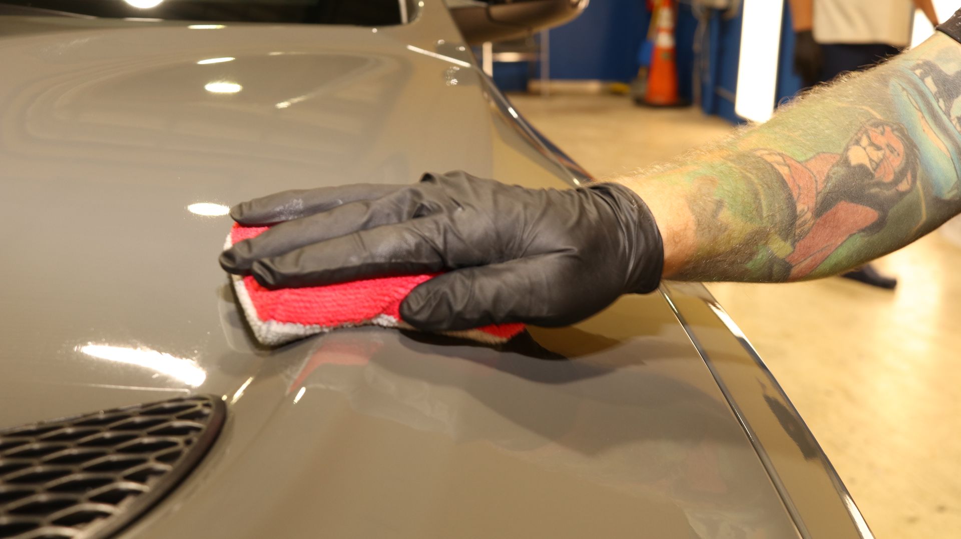 A man with a tattoo on his arm is polishing the hood of a car.