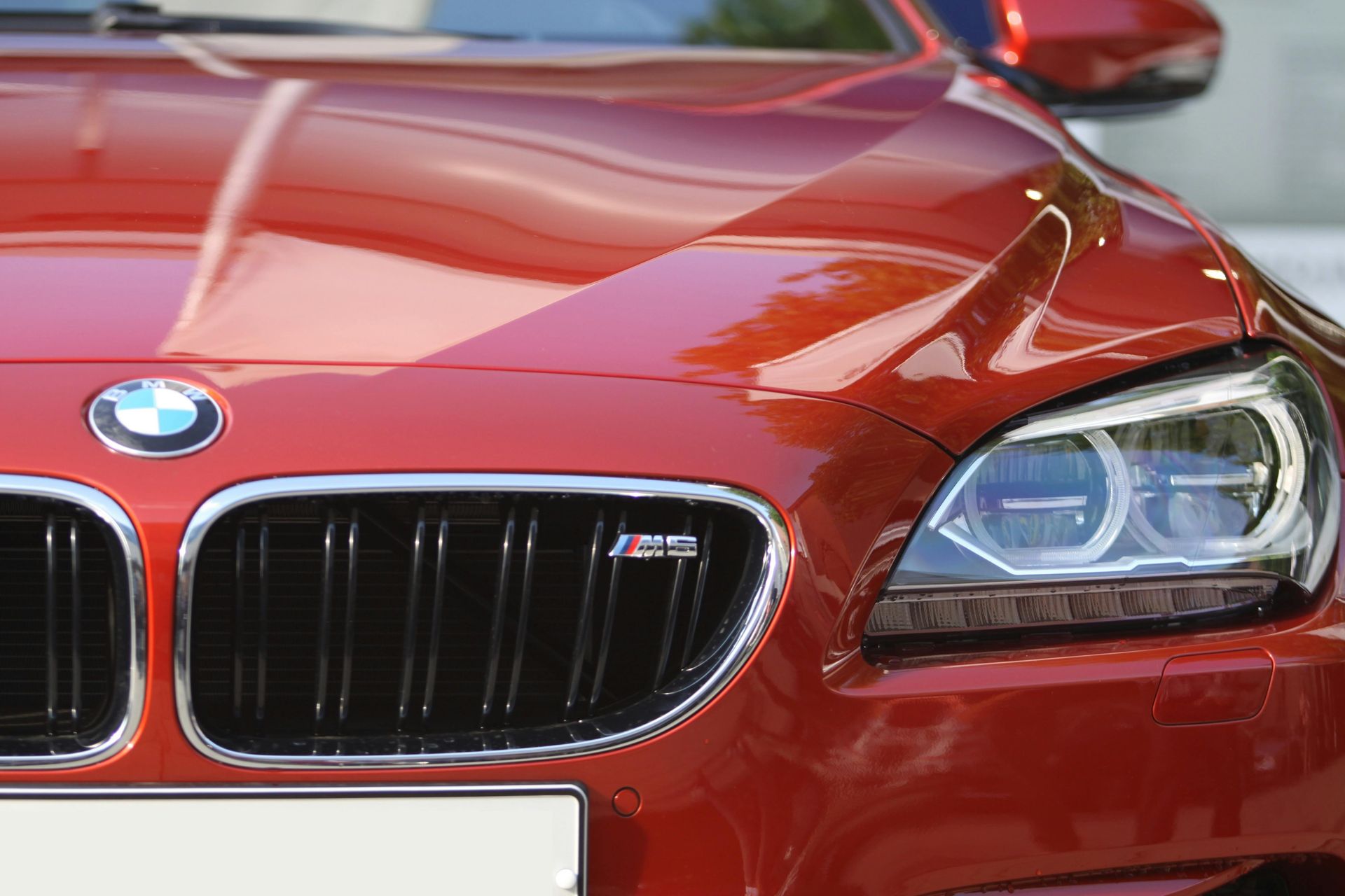 Red BMW M6 coupe's front, showing grill with M badge, headlight, and hood.