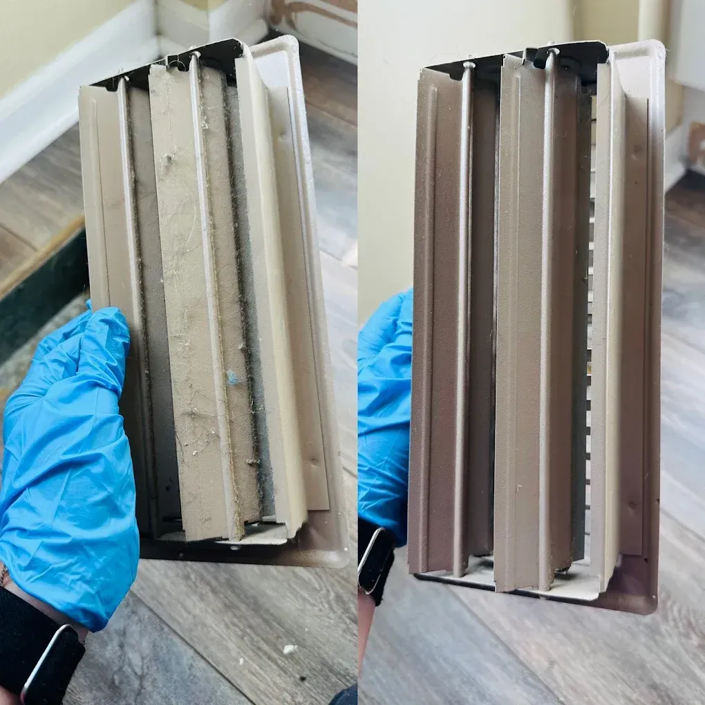 Hand in a blue glove holding a dirty air vent (left) next to a clean one (right) on wooden floor.