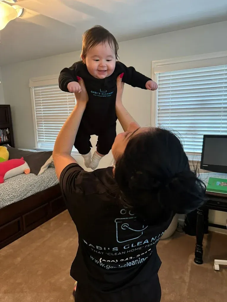 Woman holding a smiling baby in the air. They are in a bedroom.