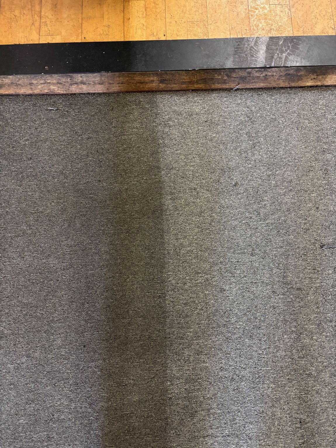 Gray textured flooring with a dark wooden trim at the top, against a yellow surface.