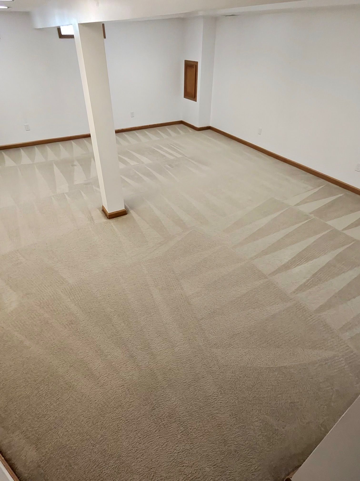 Neutral-toned basement with freshly cleaned carpet, white walls, and a support column.