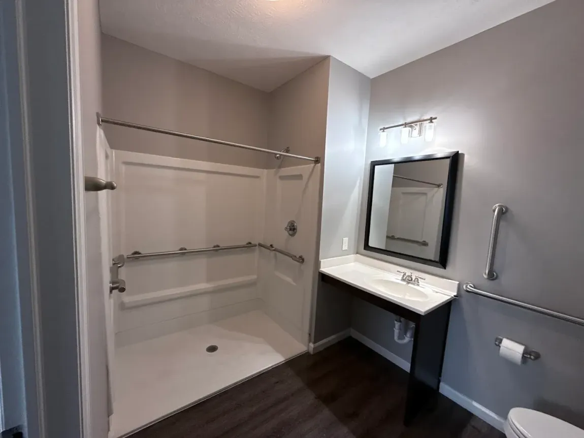 Accessible bathroom with a roll-in shower, dark floor, gray walls, and grab bars.