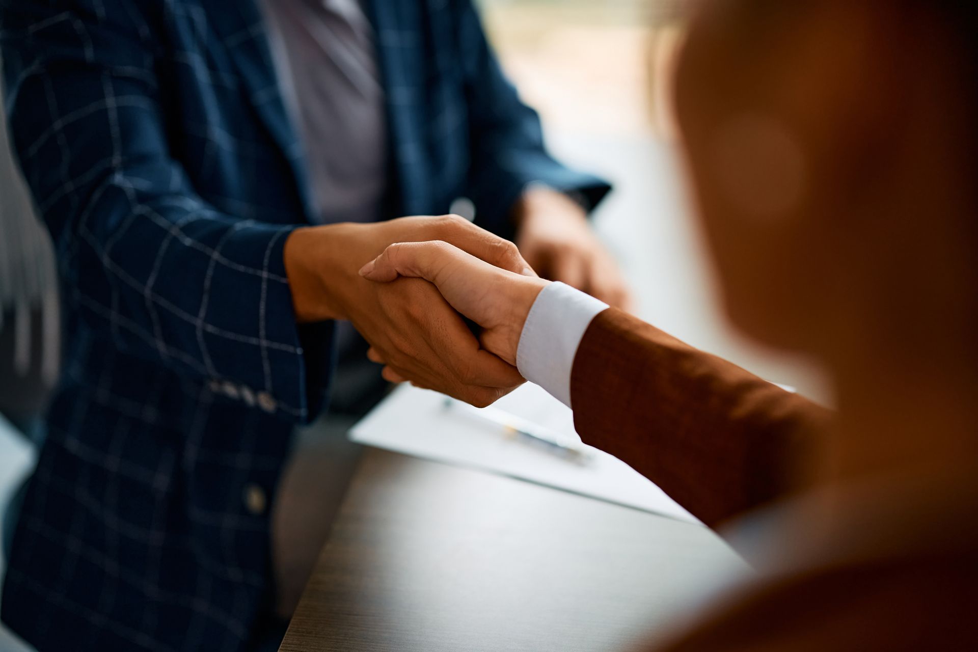 Two professionals shake hands over a desk, signifying an agreement or successful meeting.