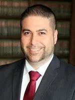 A man in a suit and tie is smiling in front of a bookshelf.