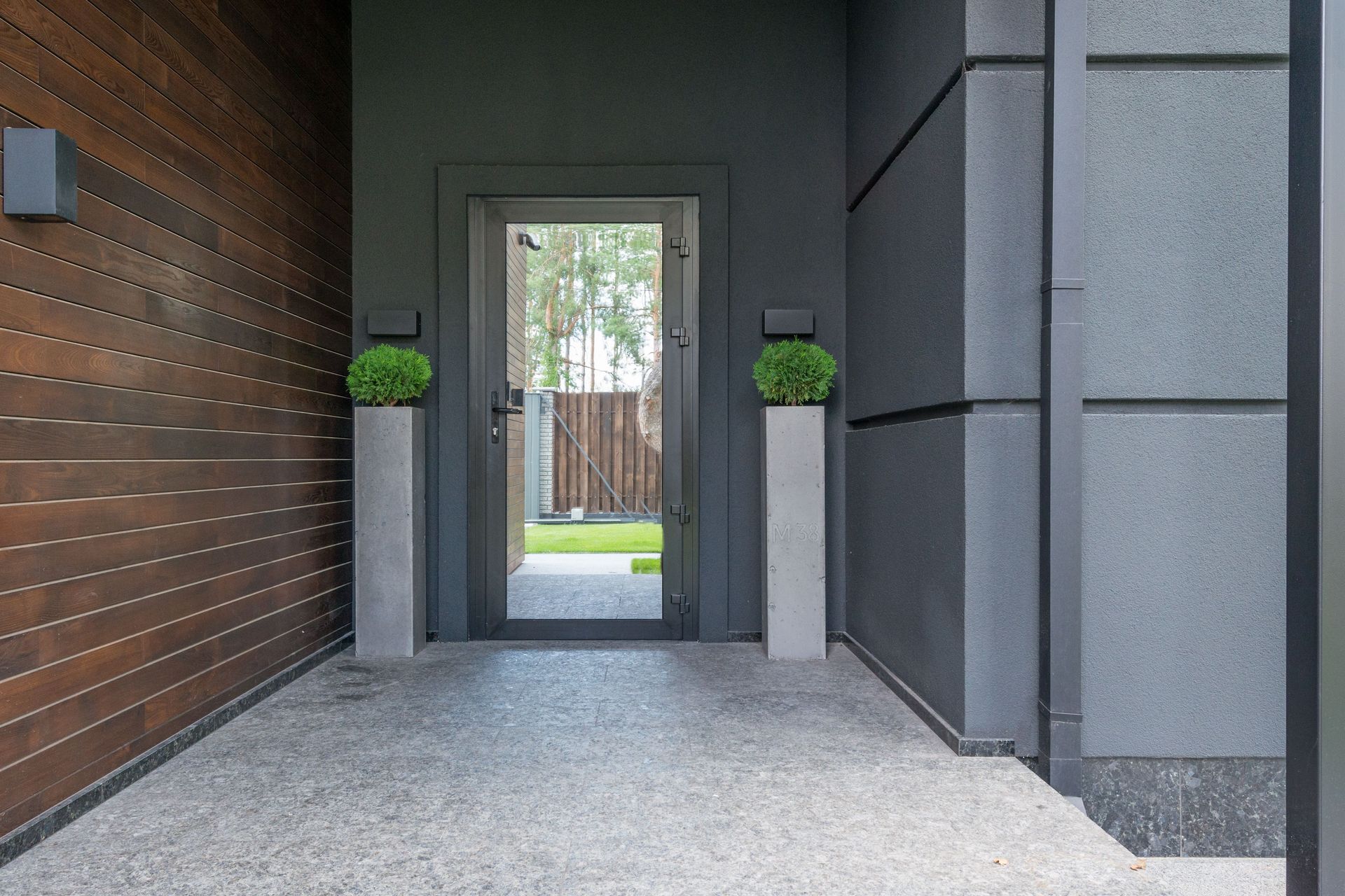 Modern home entryway with a wood wall, gray columns, and a glass door leading to a courtyard