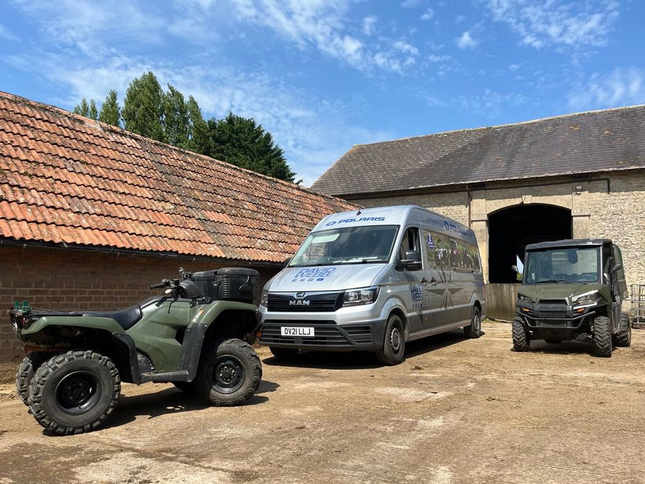 A van and an atv are parked in front of a barn.