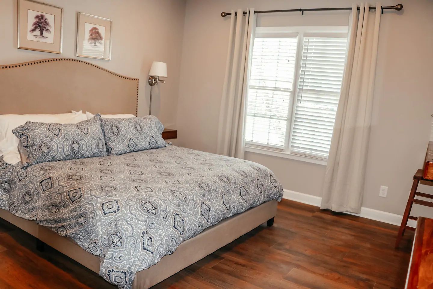 Bedroom with a bed, patterned bedding, window, lamp, and wood floor