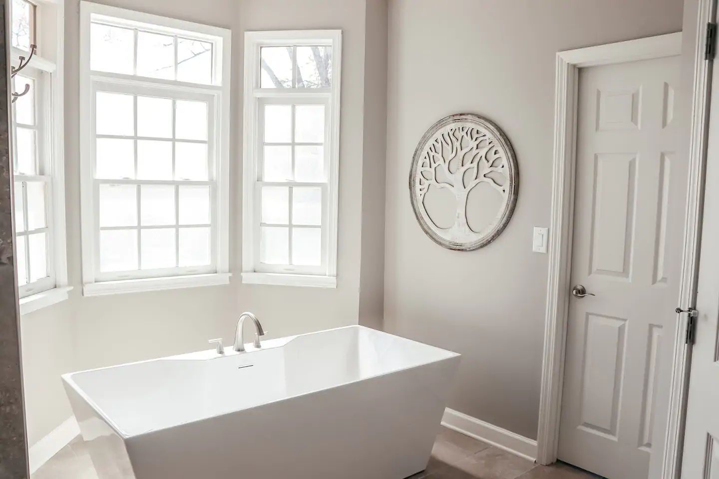 Bright bathroom with a white freestanding tub, large windows, and a round wall mirror