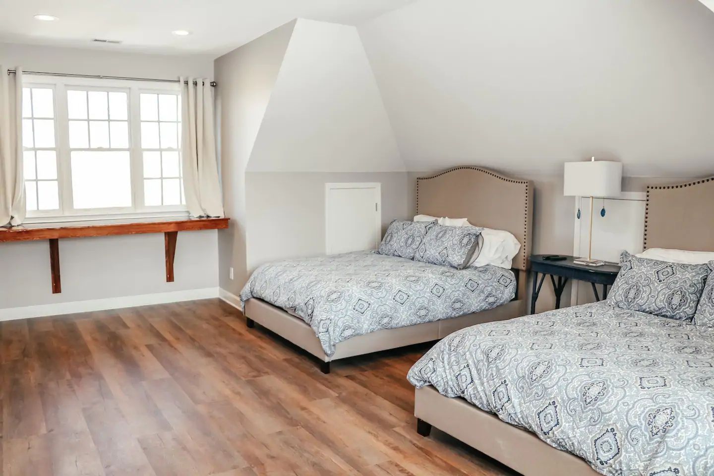 Bright bedroom with two twin beds, wooden floor, and a window seat by a large window.