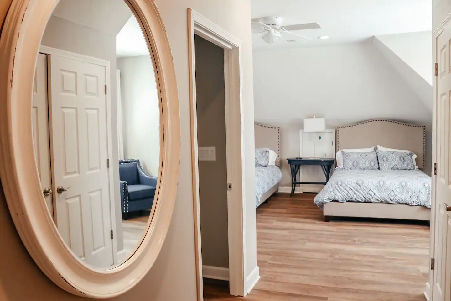 Bright bedroom with twin beds, a round mirror, and a doorway to a sitting area
