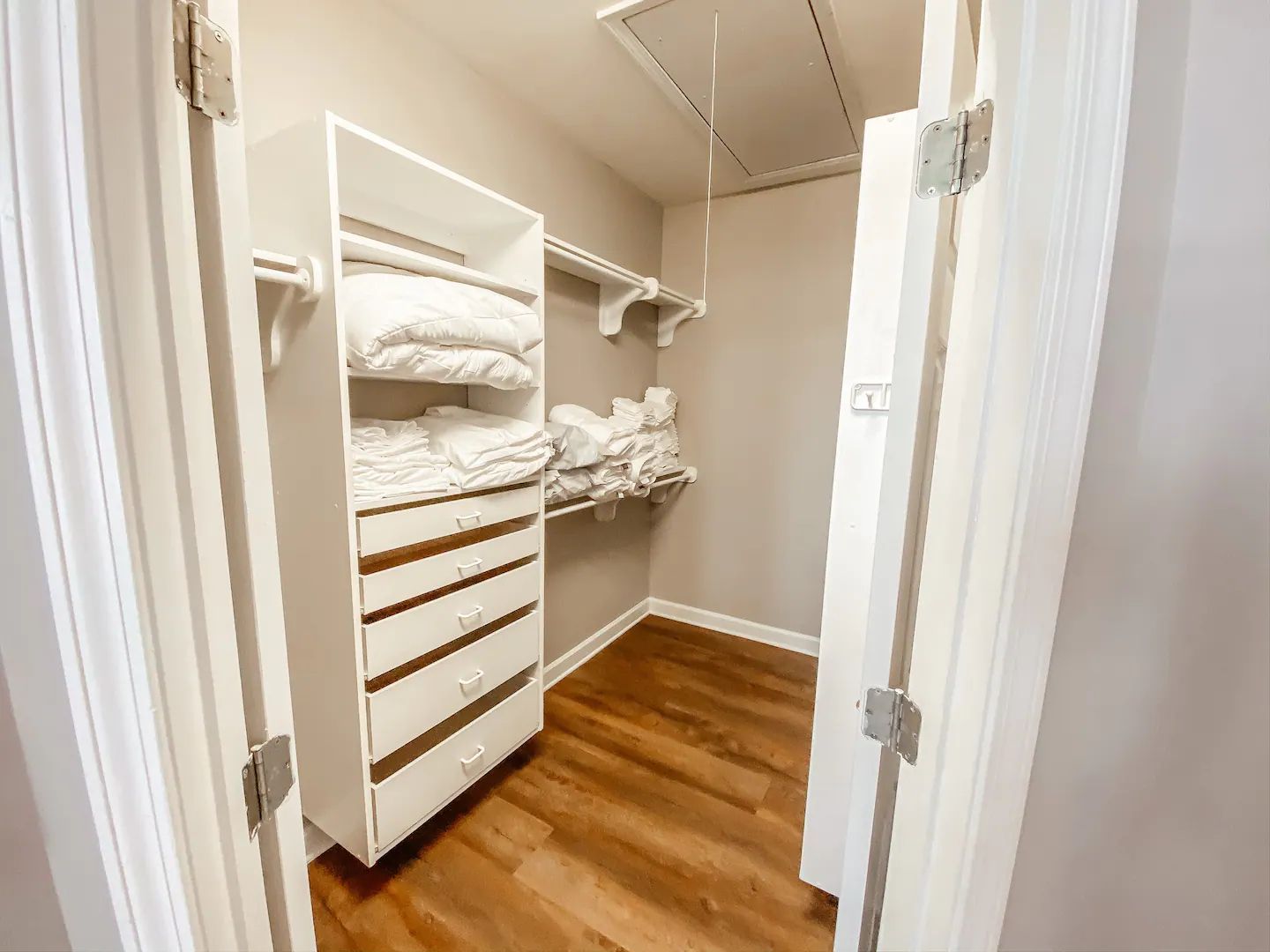 Walk-in closet with white shelving, drawers, hanging rods, folded towels, and wood flooring