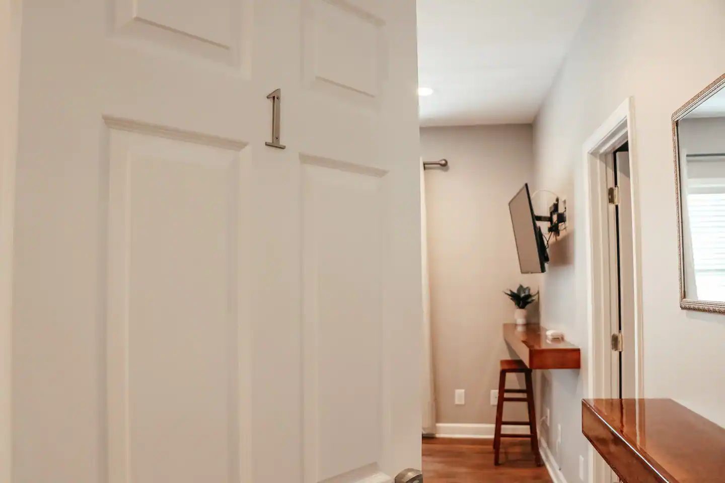 Hallway with a white open door, mirror, console table, stool, and staircase in the background.